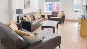 Ein modernes Wohnzimmer mit Ledersofas, einem Holztisch und Blick auf die Straße durch ein Fenster.