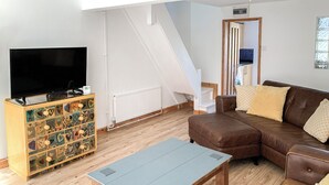 Ein Wohnzimmer mit braunem Ledersofa, einem Holztisch, einem Fernseher auf einer Holzkommode und einer weißen Treppe.