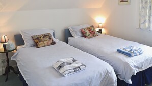A twin room with two beds, each with a pillow and a lamp. There is a small table with a lamp and a picture on the wall.