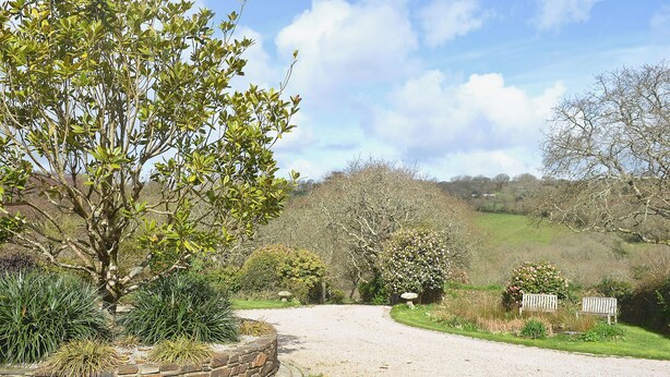 A gravel driveway leading to a house with a stone wall and a bench.