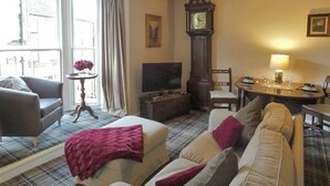 Un salon comprenant un canapé, un fauteuil, une télévision, une horloge et une table à manger.