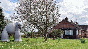 Un jardin agrémenté d’une grande sculpture d’éléphant, d’un arbre en fleurs et d’une maison à l’extérieur en briques.