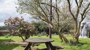 Une table de pique-nique dans un jardin où les arbres sont en fleurs, avec une grande sculpture d’éléphant.