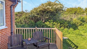 A wooden deck with two benches and a table, surrounded by a wooden fence and lush greenery. - 1 bedroom accommodation in Happisburgh (Happisburgh)