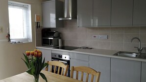 A modern kitchen with grey cabinets, a stainless steel range hood, a microwave, and a dishwasher. There is a wooden dining table with a vase of tulips. - 1 bedroom accommodation in Happisburgh (Happisburgh)