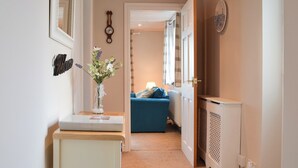 A hallway with a wooden ceiling, a white door, a blue sofa, and a small table with a vase of flowers. - 2 bedroom accommodation in Dulas, Anglesey (Dulas, Anglesey)