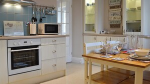 A kitchen with a microwave, oven, and a dining table set with plates and glasses. - 2 bedroom accommodation in Dulas, Anglesey (Dulas, Anglesey)