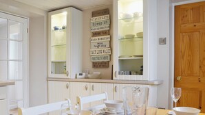 A dining area with a wooden table set for a meal, white chairs, and a kitchen area with cabinets and a refrigerator. - 2 bedroom accommodation in Dulas, Anglesey (Dulas, Anglesey)