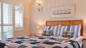 A bedroom with a large bed, wooden headboard, and a view of the outdoors through a window with blinds. - 2 bedroom accommodation in Dulas, Anglesey (Dulas, Anglesey)