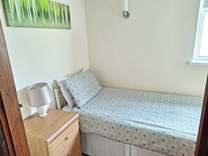Een kleine eenpersoonskamer met een houten dressoir, een lamp en een bed met een decoratief sprei.
