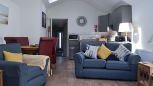 A spacious living area with a dining table, two sofas, a kitchen in the background, and a skylight above.