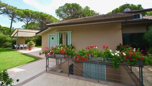 Una casa con un porche cubierto, un pequeño jardín con plantas en macetas y una escalera que lleva a la entrada.