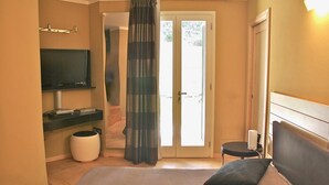 Un dormitorio con cama, televisión, una mesita y una puerta corrediza de vidrio que da a un balcón.