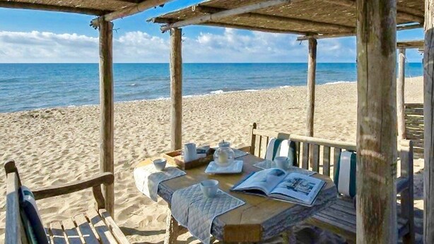 Una cabaña de madera en la playa con una mesa para dos, con vista al mar.