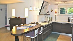Una cocina moderna con una isla central, luces colgantes y un ventanal que proporciona luz natural.