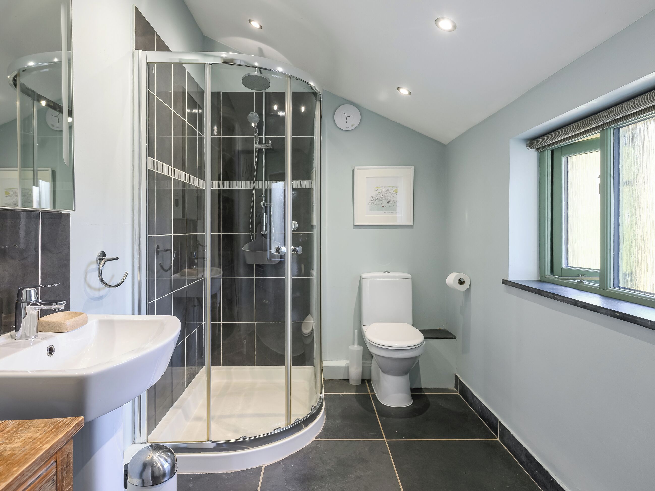 A modern bathroom with a glass-enclosed shower, a sink, a toilet, and a window.