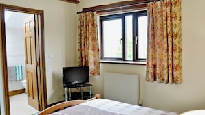 Un dormitorio con cama, televisión, ventana con cortinas y radiador.
