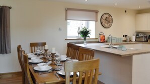 Een eetruimte met een houten tafel voor vier personen, een keuken met moderne apparaten en een grote wandklok.