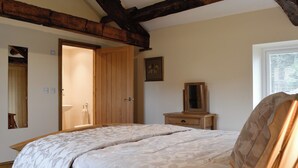 Een slaapkamer met een groot bed, een houten garderobe en een klein nachtkastje met spiegel.