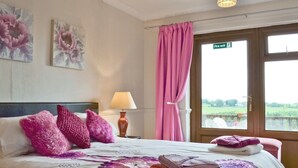 A hotel room with a bed, pillows, a lamp, a window with a view, and a fire exit sign.
