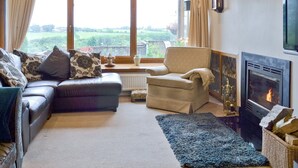 A cozy living room with a fireplace, a sofa, a chair, and a view of the outdoors.