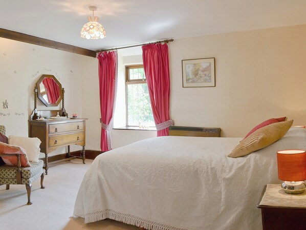 A bedroom with a bed, a dresser, a mirror, a window with curtains, and a radiator. - Forget Me Not Cottage (New Radnor, near Hay-on-Wye)