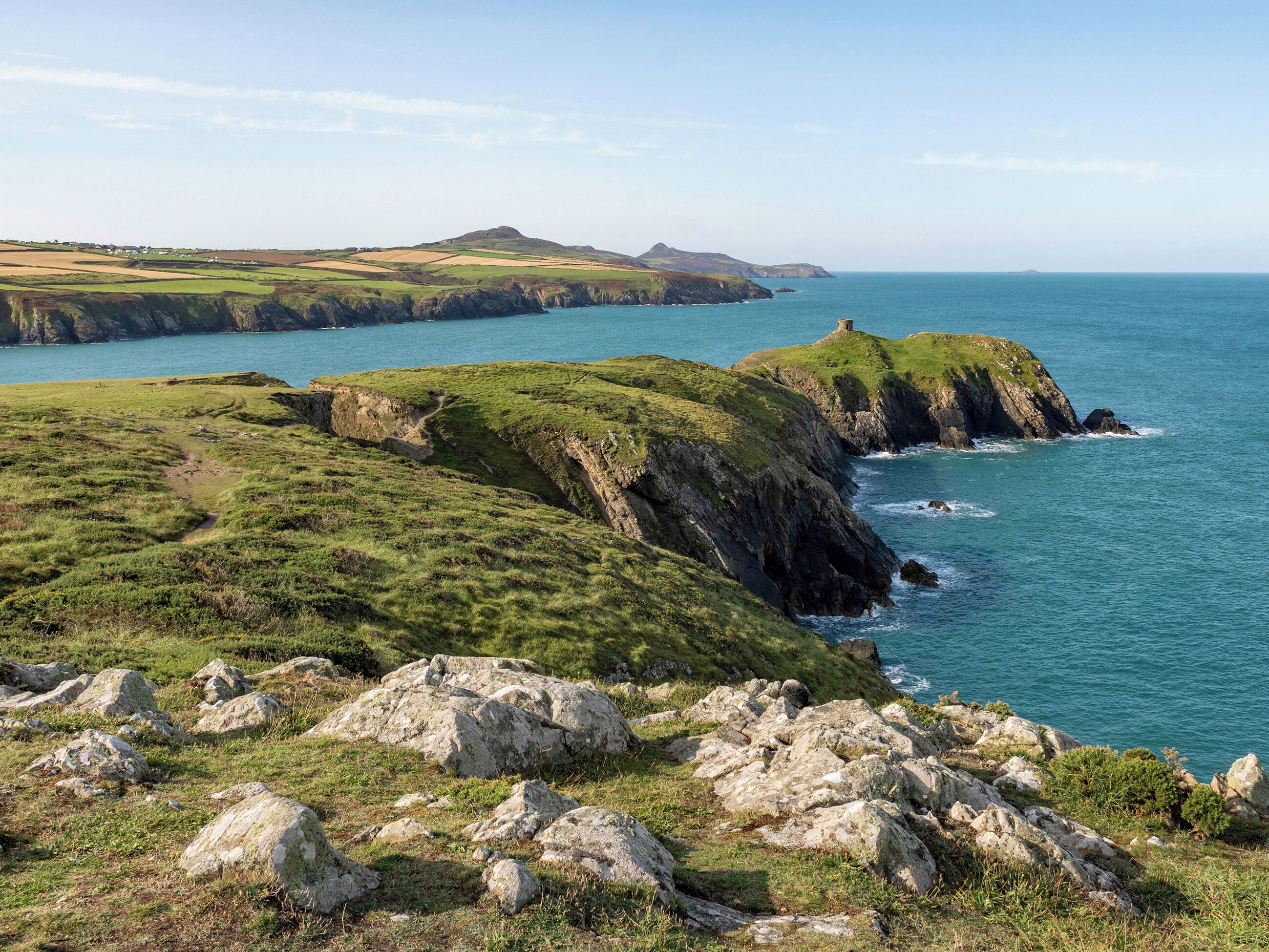 A coastal landscape with rocky terrain and grassy hills.