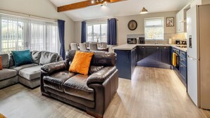 A modern kitchen with a central island, a dining area with a table and chairs, and a living room with a leather sofa and a fireplace. - Humphrey-Basil Lodge-UKC2176 (Norton Disney, near Lincoln)