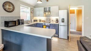A modern kitchen with a central island, built-in appliances, and a wooden ceiling beam. - Humphrey-Basil Lodge-UKC2176 (Norton Disney, near Lincoln)