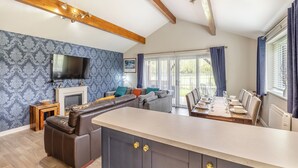 A modern living room with a fireplace, a large sofa, a dining area, and a TV mounted on the wall. - Humphrey-Basil Lodge-UKC2176 (Norton Disney, near Lincoln)