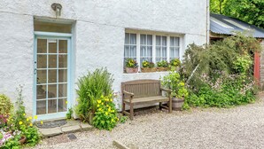 A white cottage with a blue door, a bench, and flower boxes on the windowsills. - 1 bedroom accommodation in Lyth, near Wick (Lyth, near Wick)