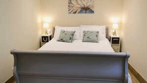 Una cama bien hecha con dos almohadas, dos mesitas de noche con lámparas y un cuadro de una flor colgado en la pared.
