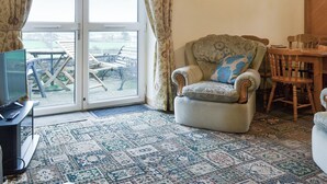 A living room with a patterned carpet, a sofa, a chair with a cushion, a television, and a table with chairs.