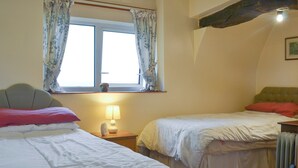 A bedroom with two beds, a window with curtains, a bedside lamp, and a radiator.