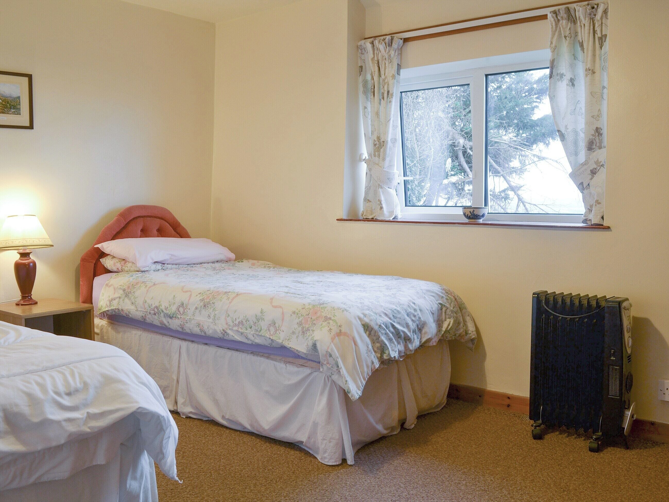 A bedroom with a single bed, a nightstand with a lamp, a radiator, and a window with curtains.