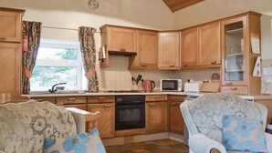 A compact kitchen with wooden cabinets, a microwave, a toaster, and a sink. There are two upholstered chairs with floral patterns.