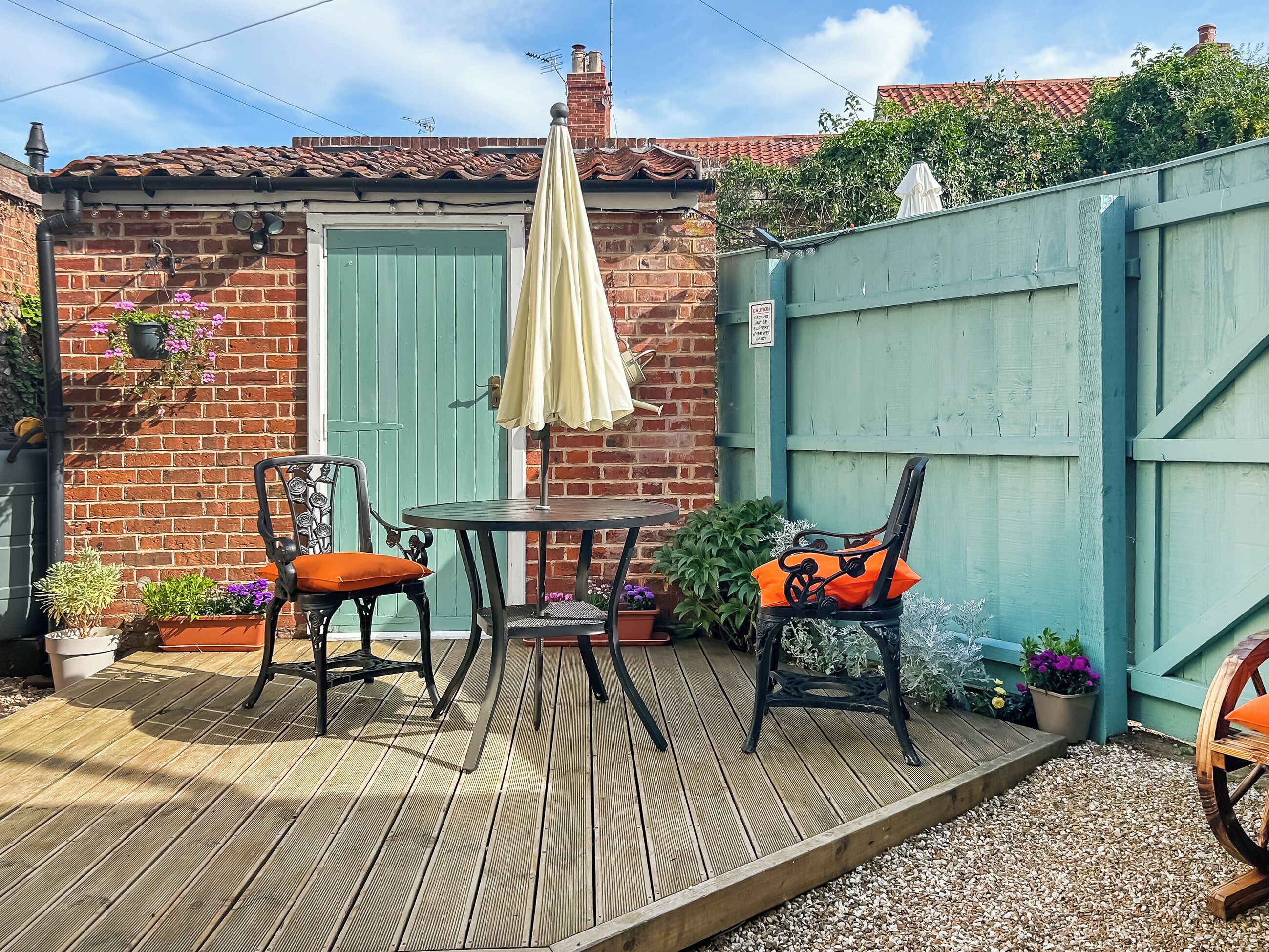 A wooden deck with two chairs and a table, a green door, and a blue fence.