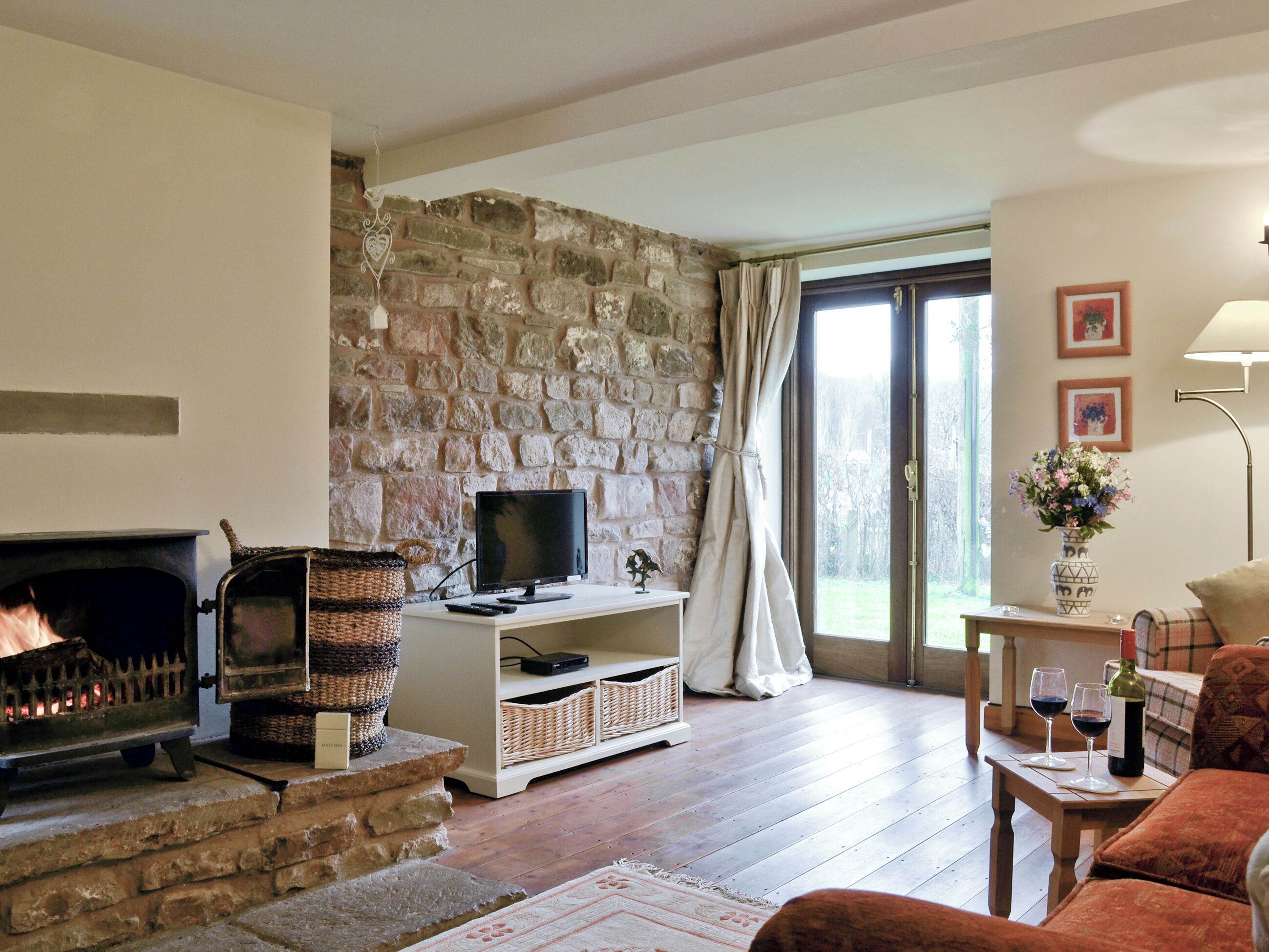 A cozy living room with a stone wall, a fireplace, a television, and a dining area with a table and chairs.