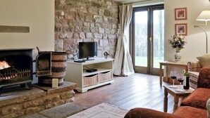 A cozy living room with a stone wall, a fireplace, a television, and a dining area with a table and chairs.