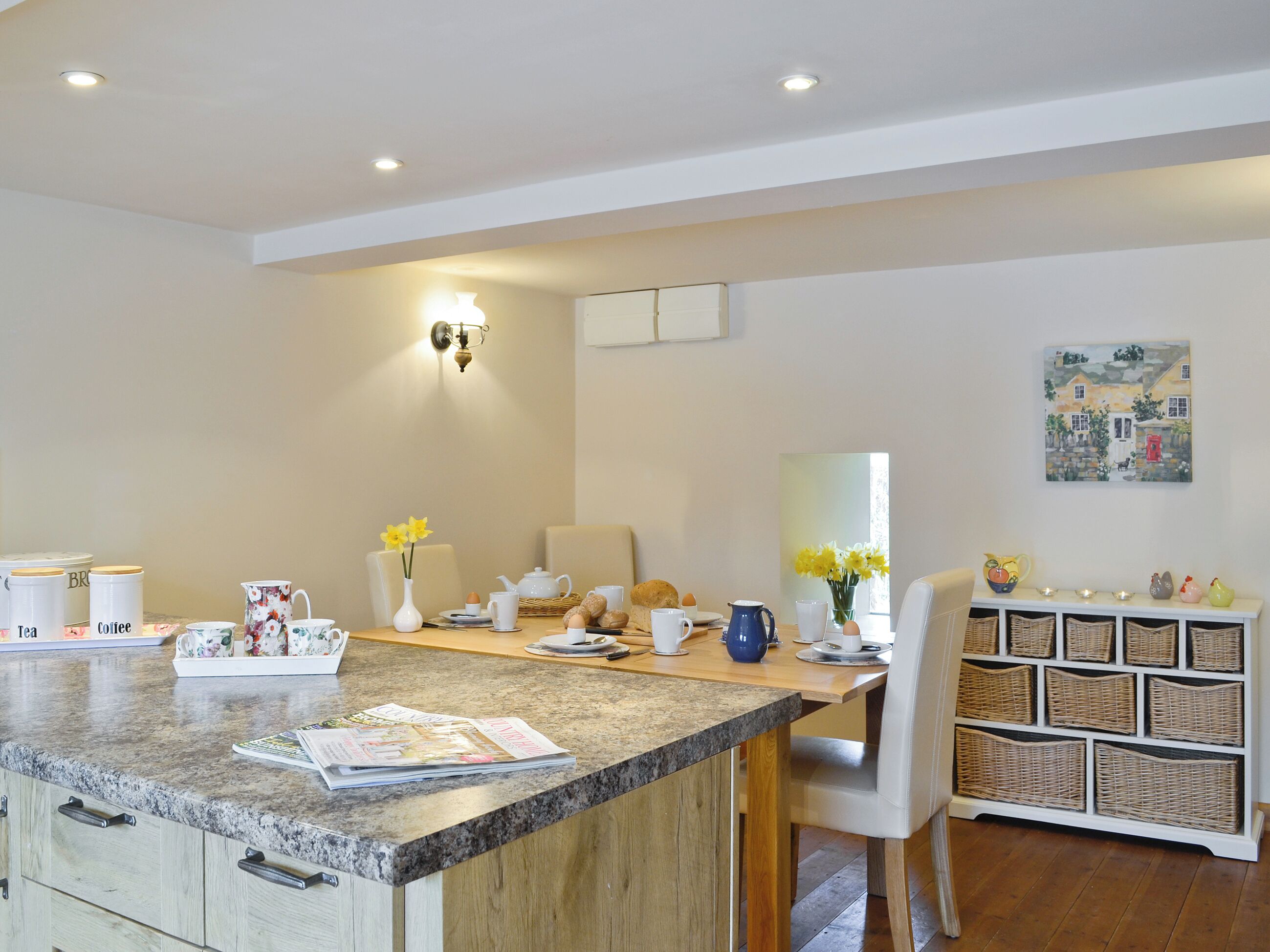 A modern kitchen with a granite countertop, a dining area with a white chair, and a wicker storage unit.
