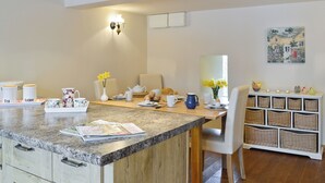 A modern kitchen with a granite countertop, a dining area with a white chair, and a wall-mounted light fixture.