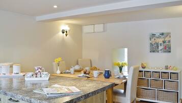 A modern kitchen with a granite countertop, a dining area with a white chair, and a wicker storage unit.