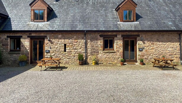 A stone building with two pitched roofs, two windows, and two chimneys.