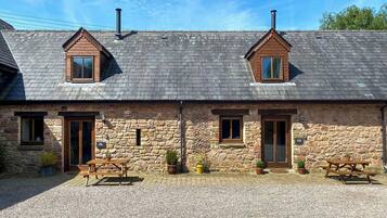 A stone building with two pitched roofs, two windows, and two chimneys.