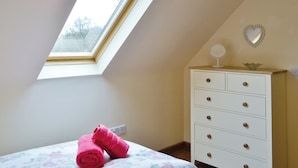 A bedroom with a skylight, a bed with floral bedding, a white dresser, and a heart-shaped mirror on the wall.