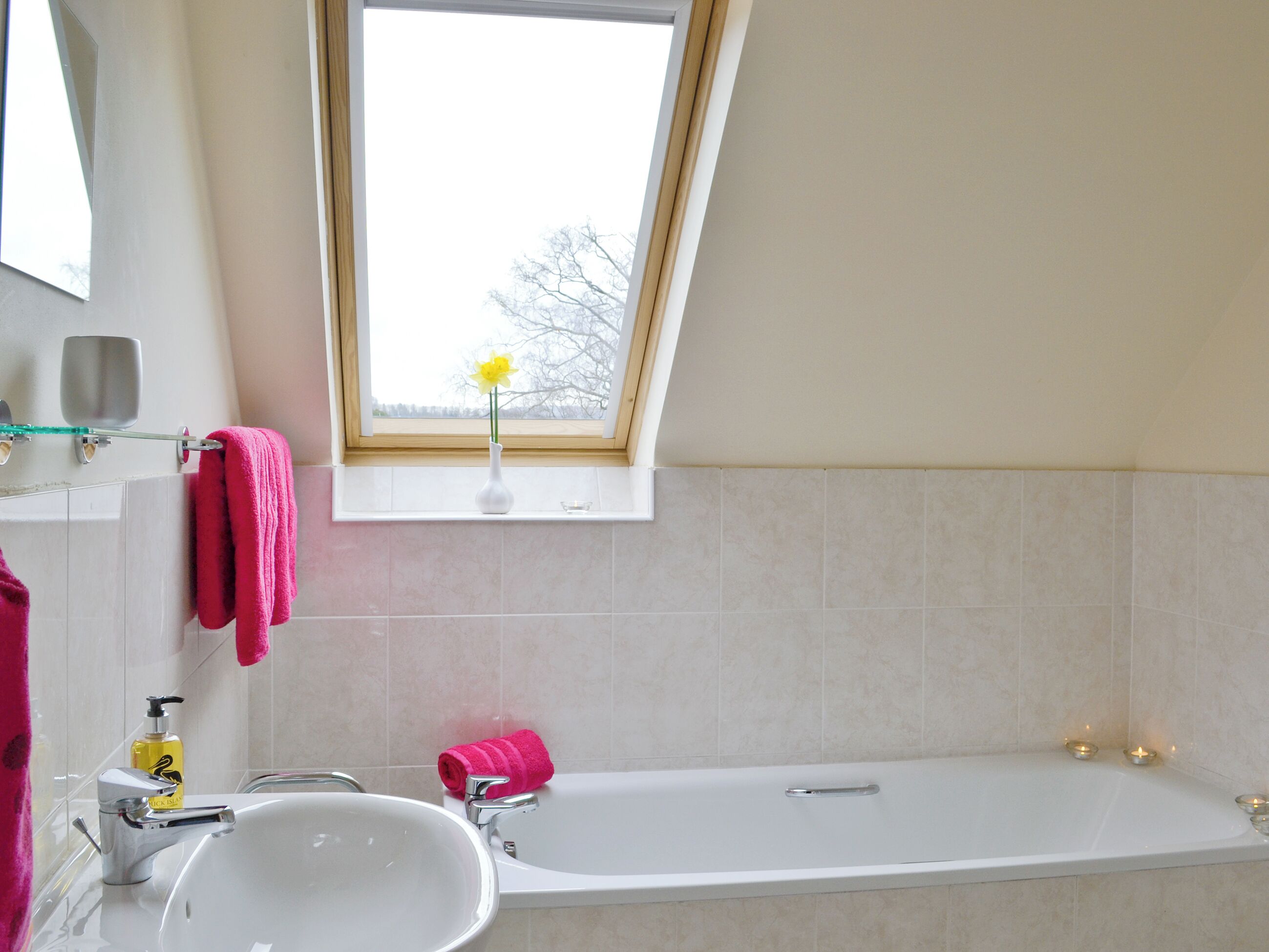 A bathroom with a white bathtub, a sink, a window with a view of trees, and a pink towel on the wall.