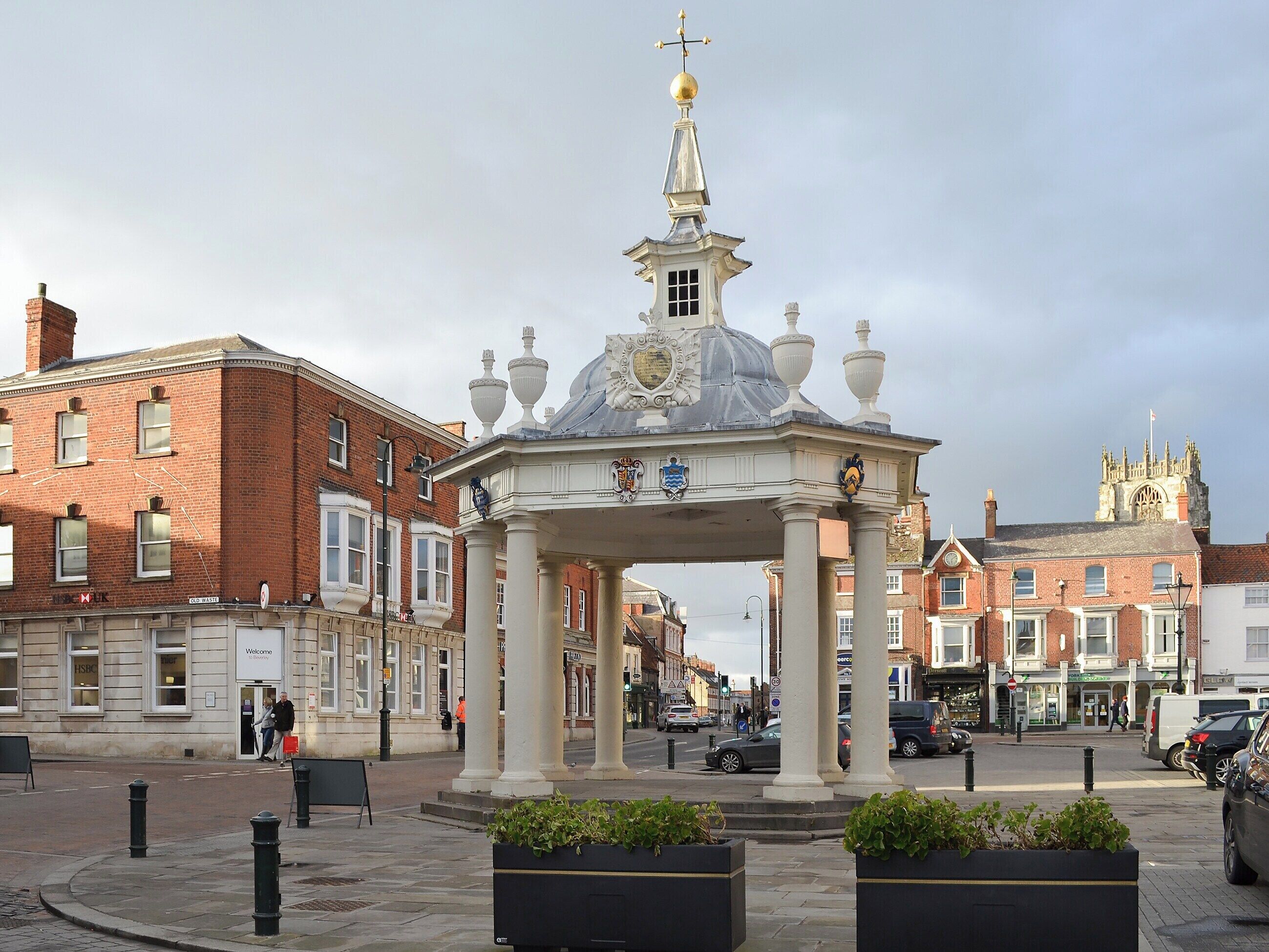 A historic pavilion with a dome and columns, surrounded by brick buildings and a church in the background.