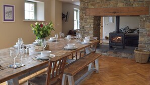 A dining area with a long wooden table set for a meal, a stone fireplace, and a cozy seating area. - 5 bedroom accommodation in Llangoedmor, near Cardigan (Llangoedmor, near Cardigan)
