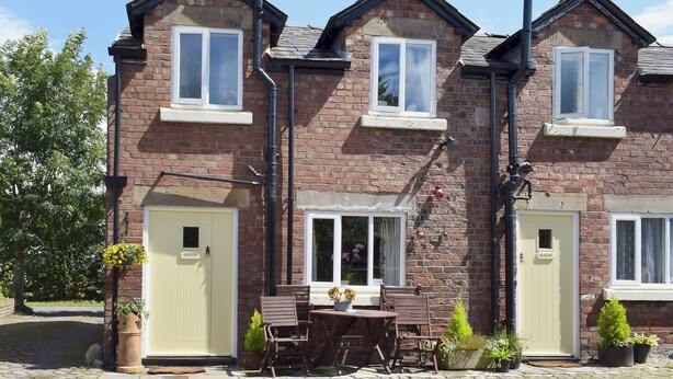 A brick house with two visible doors, a window, and a small outdoor seating area with a table and chairs. - 2 bedroom accommodation in Burscough, near Southport (Burscough, near Southport)