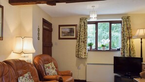 A living room with a brown leather sofa, a television, and a window with floral curtains. - 2 bedroom accommodation in Burscough, near Southport (Burscough, near Southport)